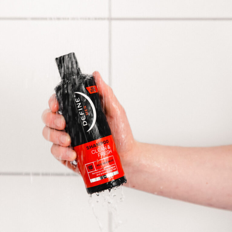 Hånd som holder svart shampooflaske foran hvite fliser