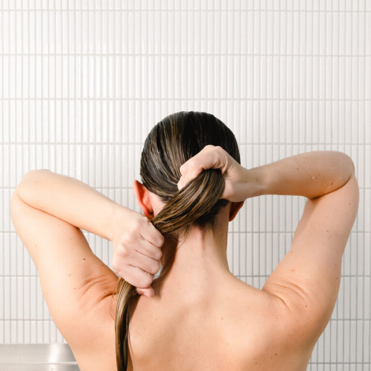 Dame sett bakfra som vasker håret i dusjen