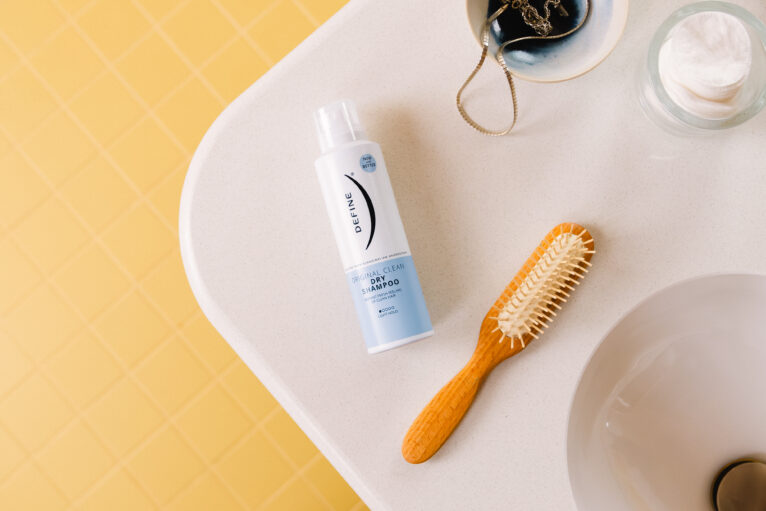 Tørrshampooflaske ligger på baderomsvasken ved siden av en hårbørste