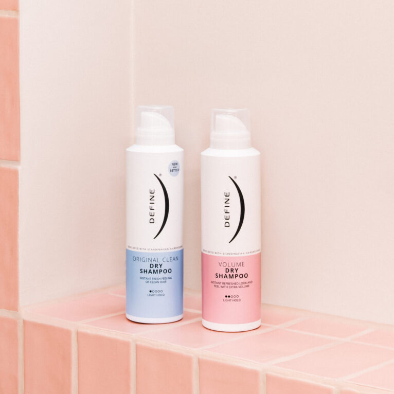 To tørrshampooflasker på rosa fliser i baderomshylle