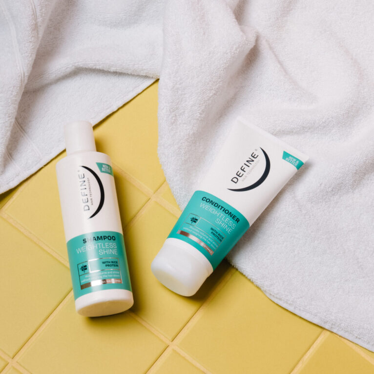 Shampoo og balsam på gule fliser, fugleperspektiv. Bak de ligger et hvitt håndkle