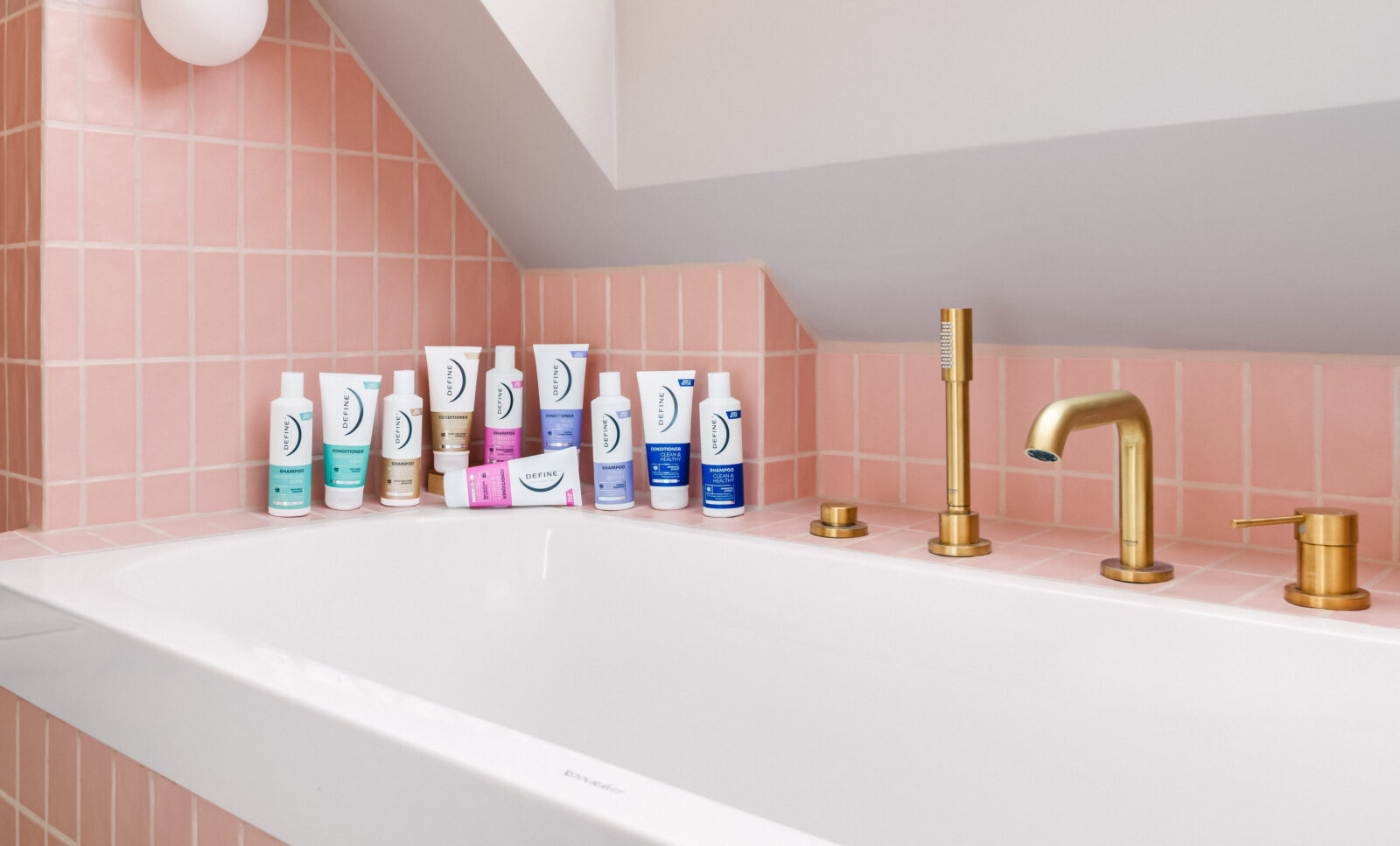 alle shampoo og balsam fra define står samlet på en badekarskant foran rosa fliser