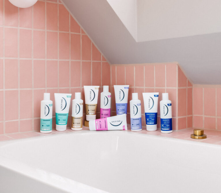 alle shampoo og balsam fra define står samlet på en badekarskant foran rosa fliser
